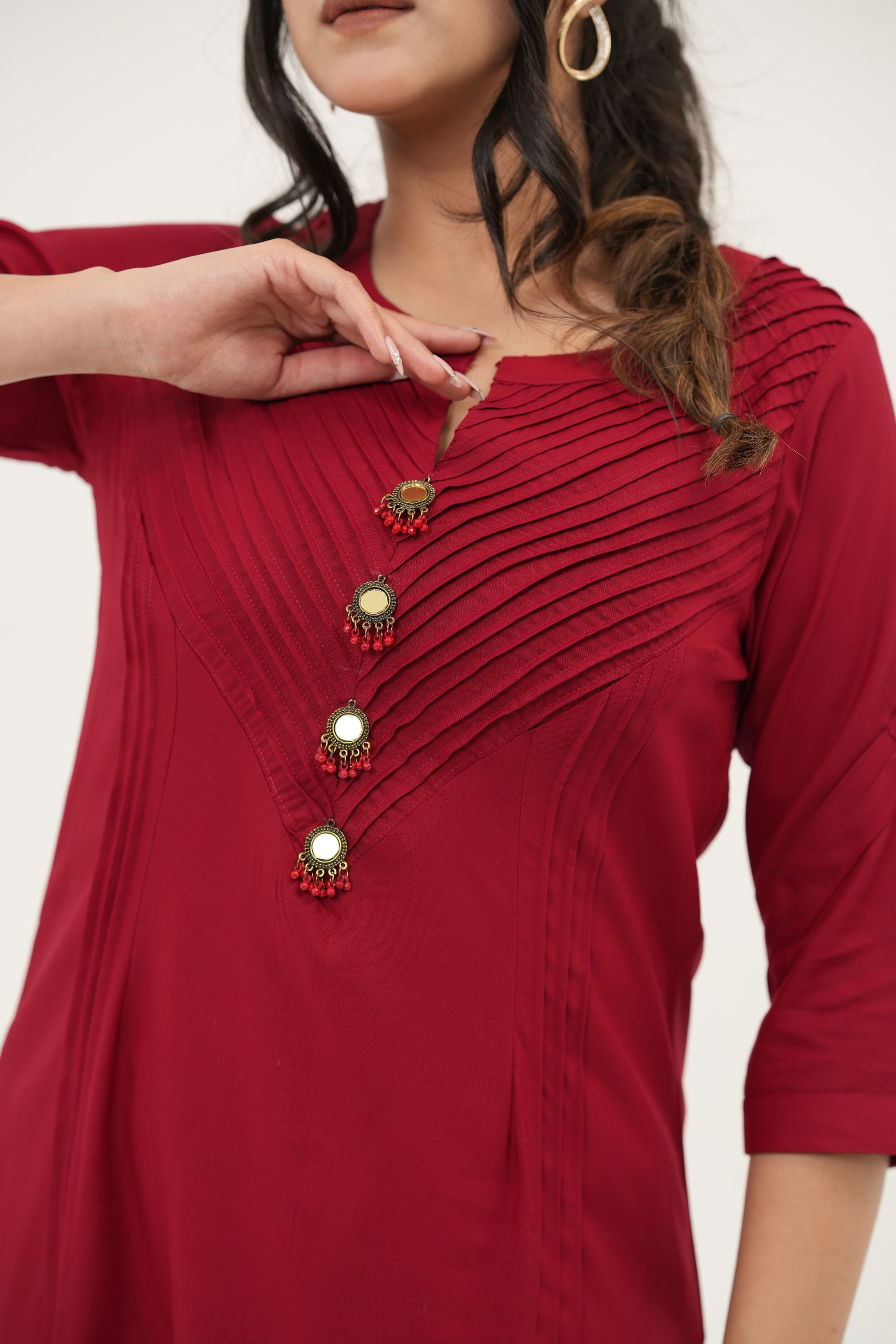 A woman wearing a Stylish red rayon viscose kurta set featuring pintuck neckline, 3/4 sleeves, and handcrafted pearl button embellishments, close-up view