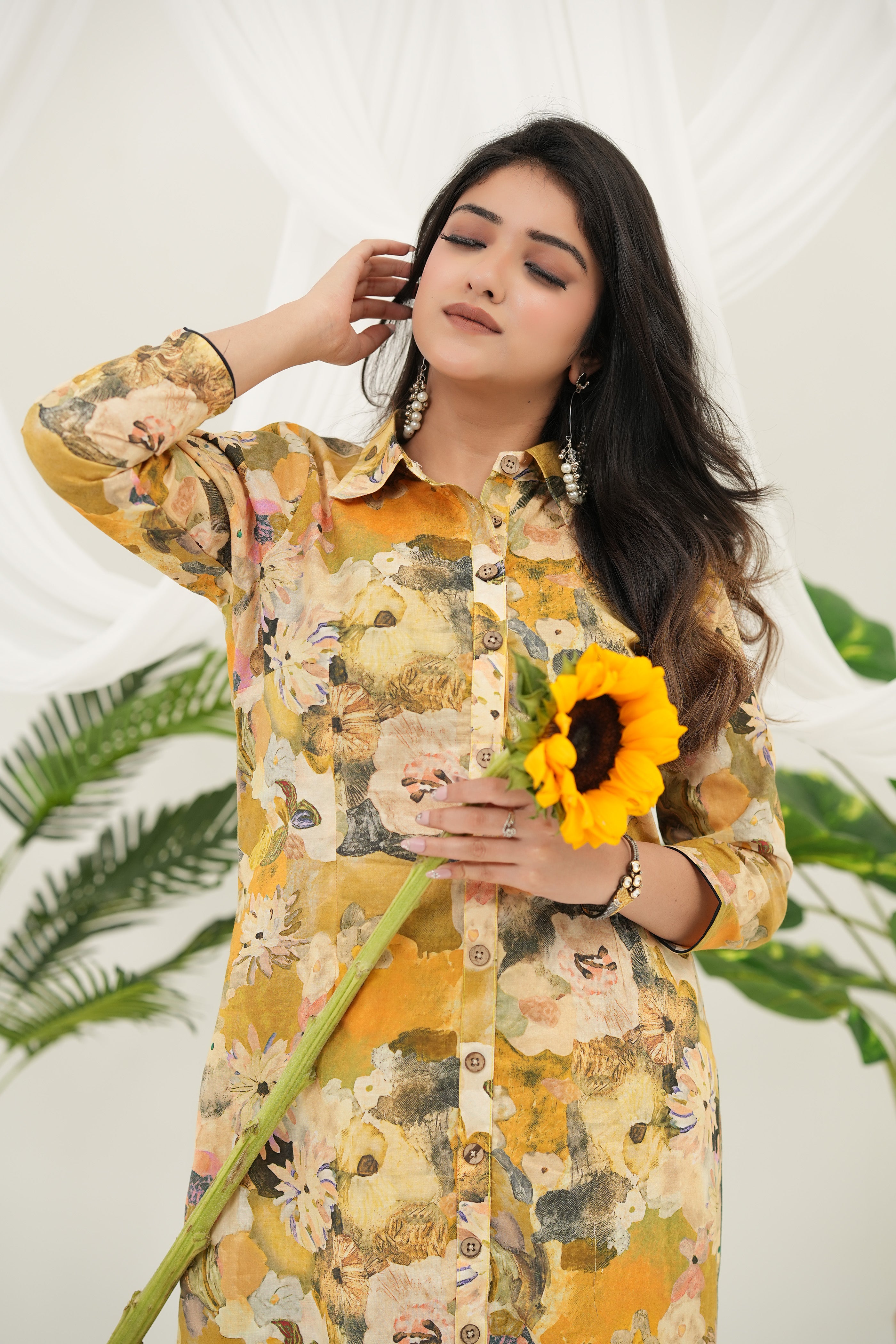 A woman wearing a Elegant yellow cotton kurta set with multicolor botanical prints, holding a sunflower – Simroz.