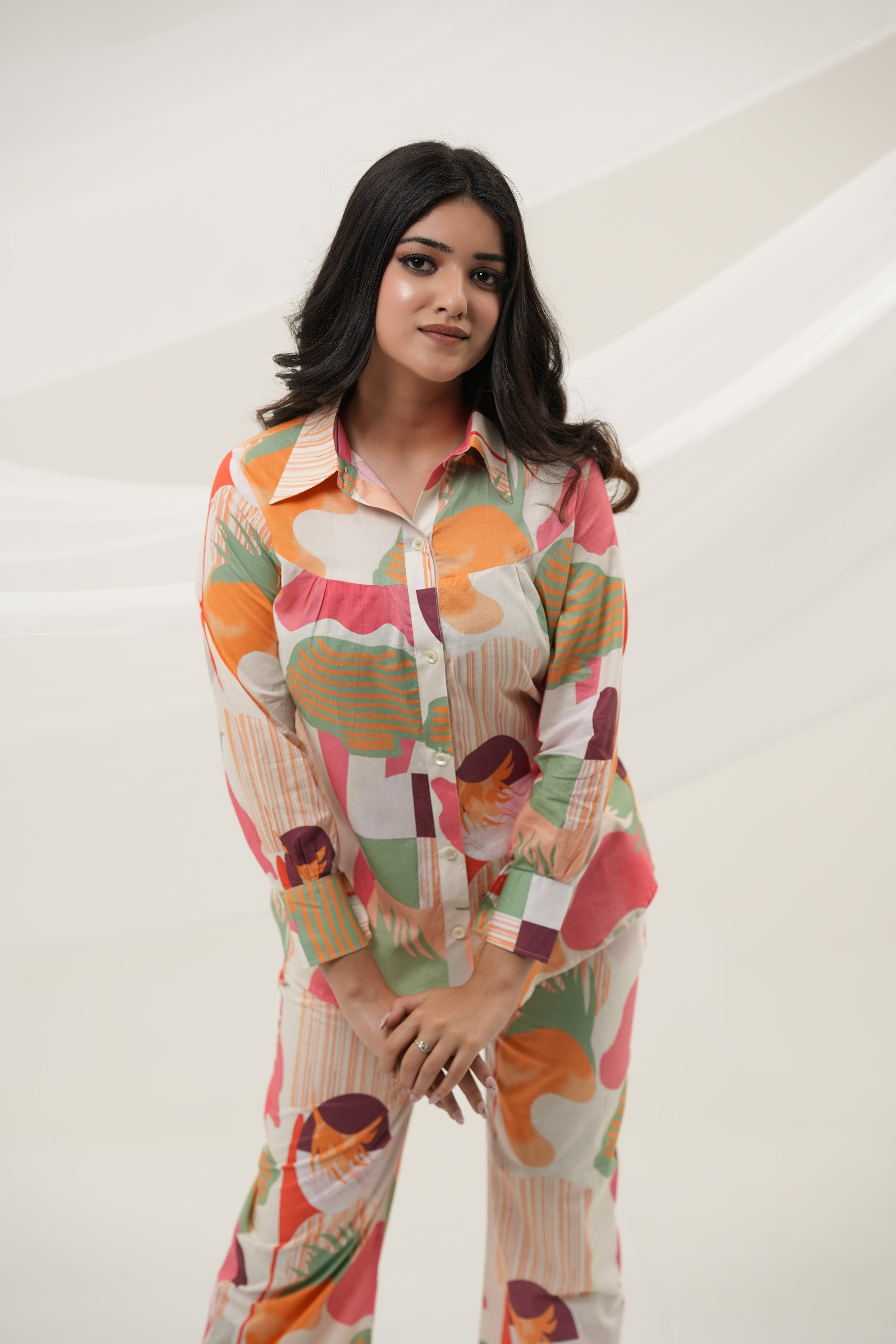 A woman is standing, bending over, wearing a multicolored abstract print co-ord set consisting of a long-sleeved top and pants - Simroz.