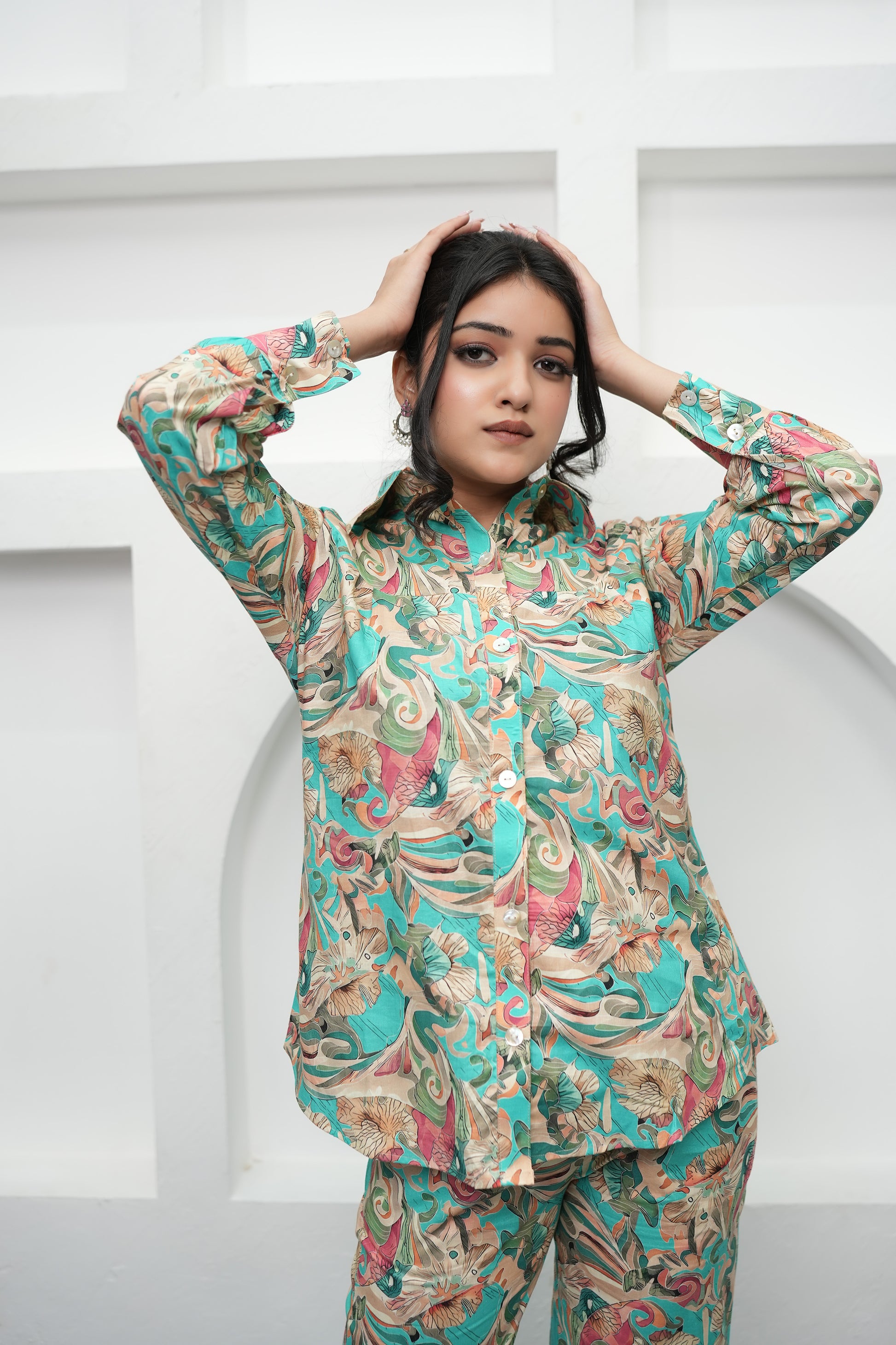 A woman is standing, hands over head, wearing a teal and beige printed co-ord set with a floral pattern - Simroz.