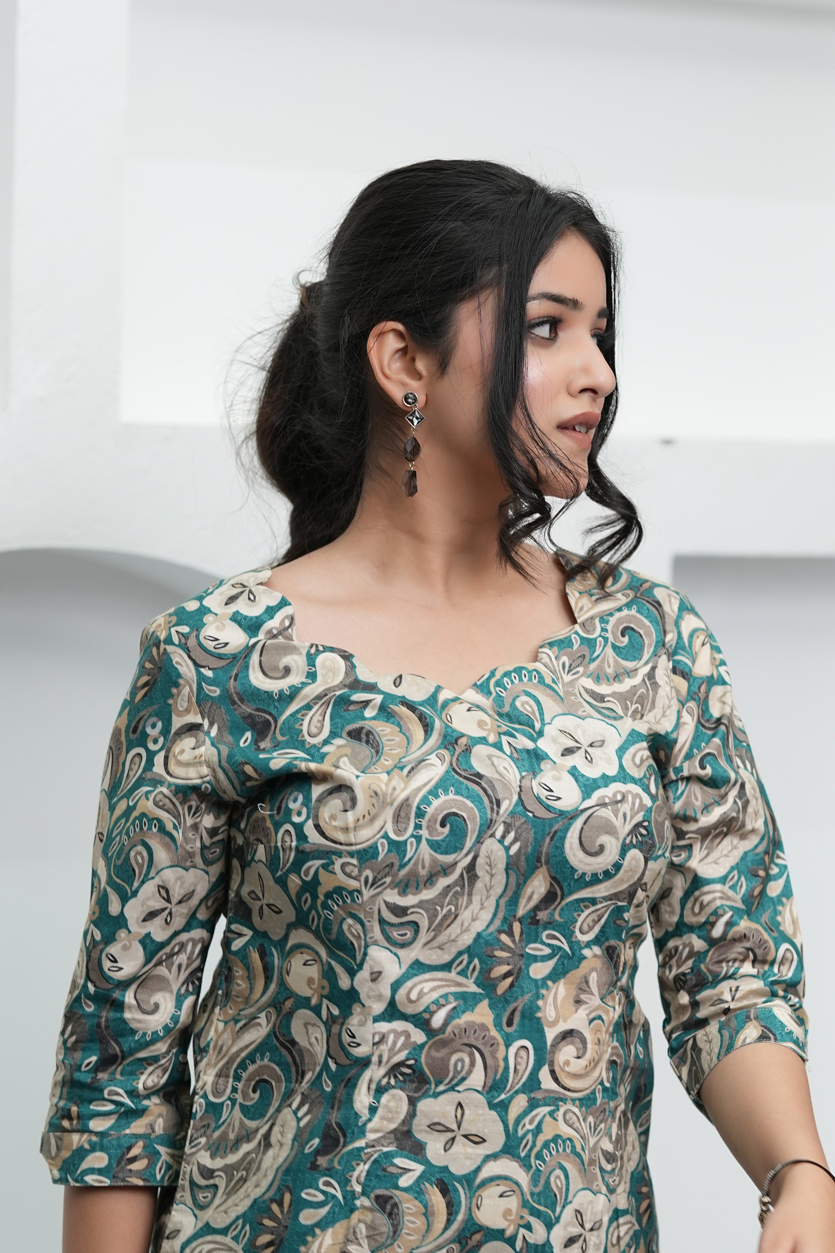 A woman wearing a paisley print tunic in deep teal, warm beige, and soft cream colors with three-quarter sleeves and a round neckline, close-up - Simroz.