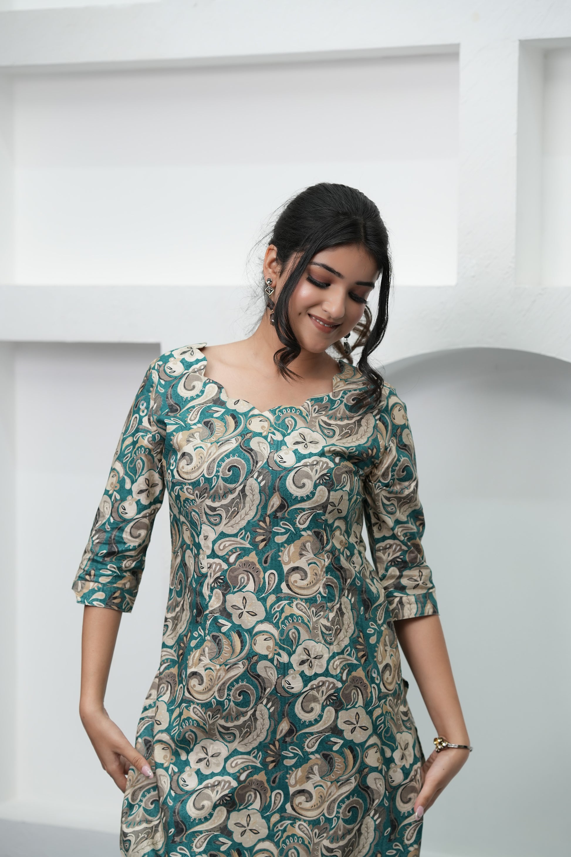 A woman wearing a paisley print tunic in deep teal, warm beige, and soft cream colors with three-quarter sleeves and a round neckline - Simroz.