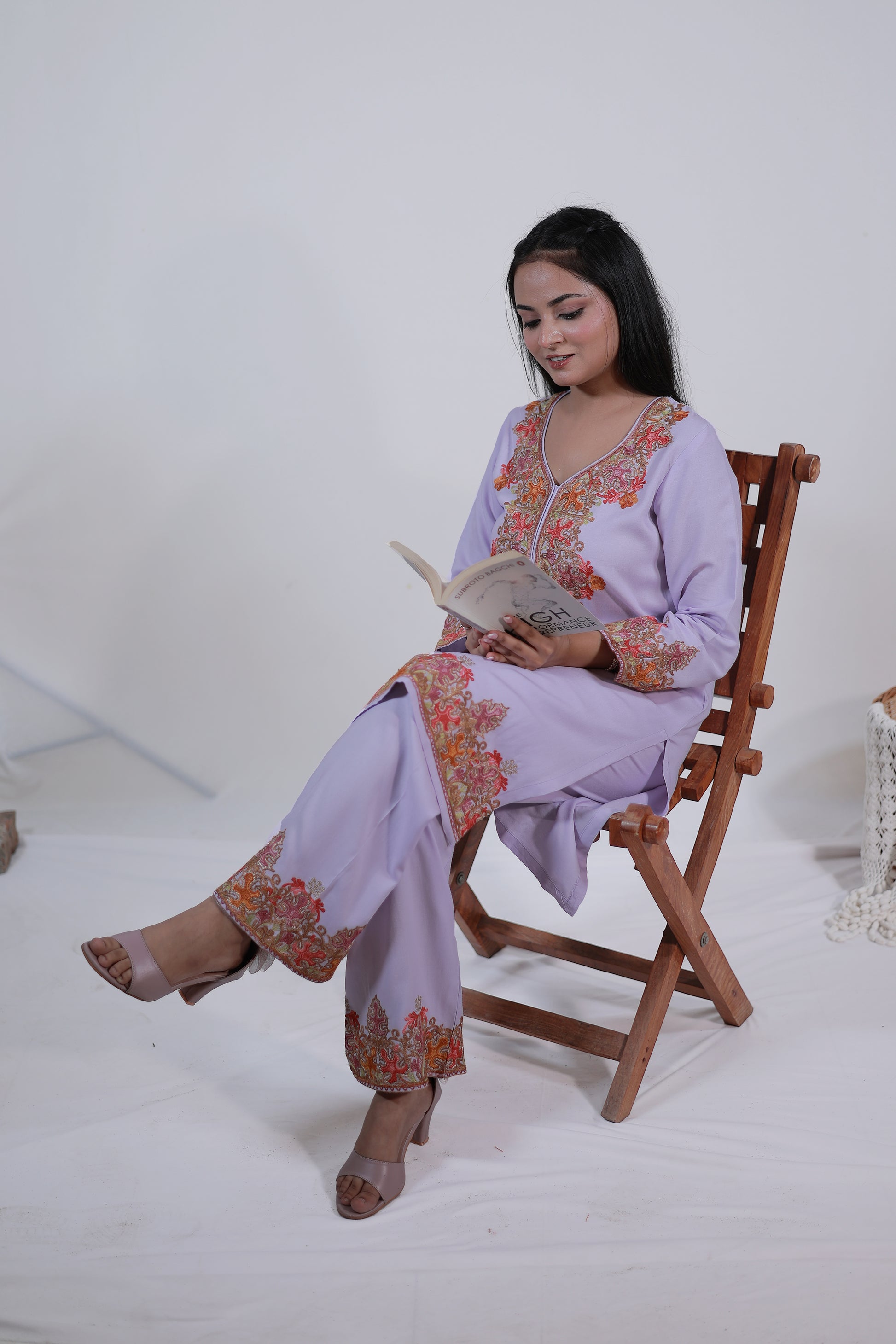 Simroz Mauve Kashmiri Embroidered Kurta Set in rayon viscose fabric, straight style festive outfit with matching bottoms, sitting on a wooden chair and reading a book